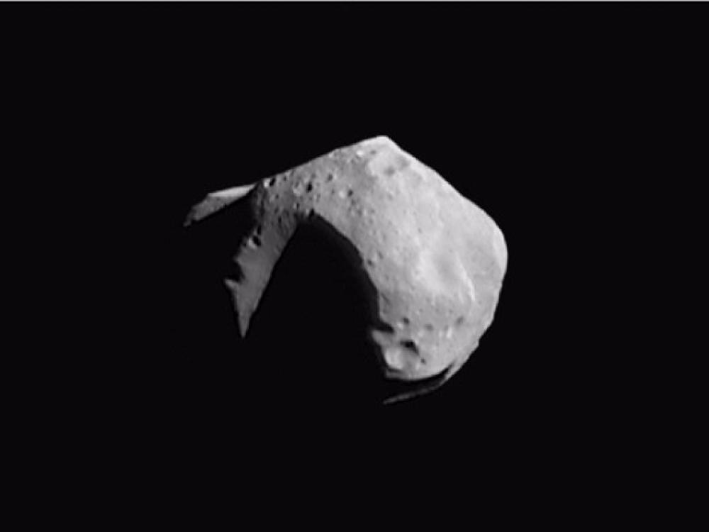 A large asteroid with many visible craters. The left side experiences a large shadow from being in the opposite direction of the sun.