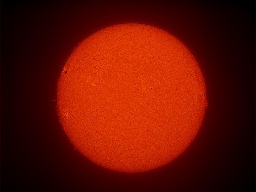 Disk view of the Sun with a large sunspot cluster visible on the left side of the Sun. 