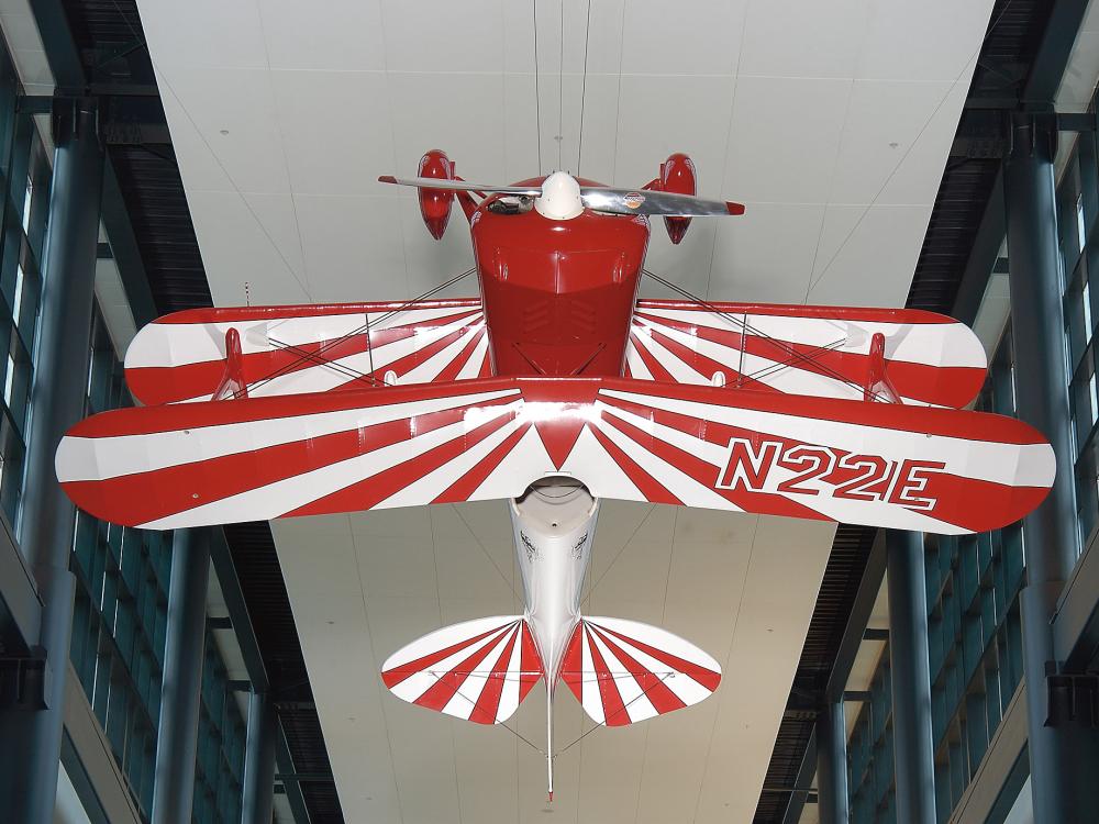 A biplane that hangs upside down, with a red body and red and white striped wings. 