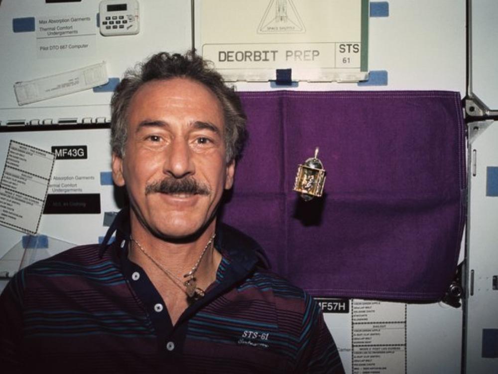 Astronaut Jeffrey Hoffman smiles next to a dreidel floating. 