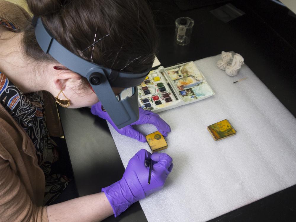 A photo of Lauren Gottschlich, Engen Conservation Fellow, inpainting the losses on the lid with watercolor paints.