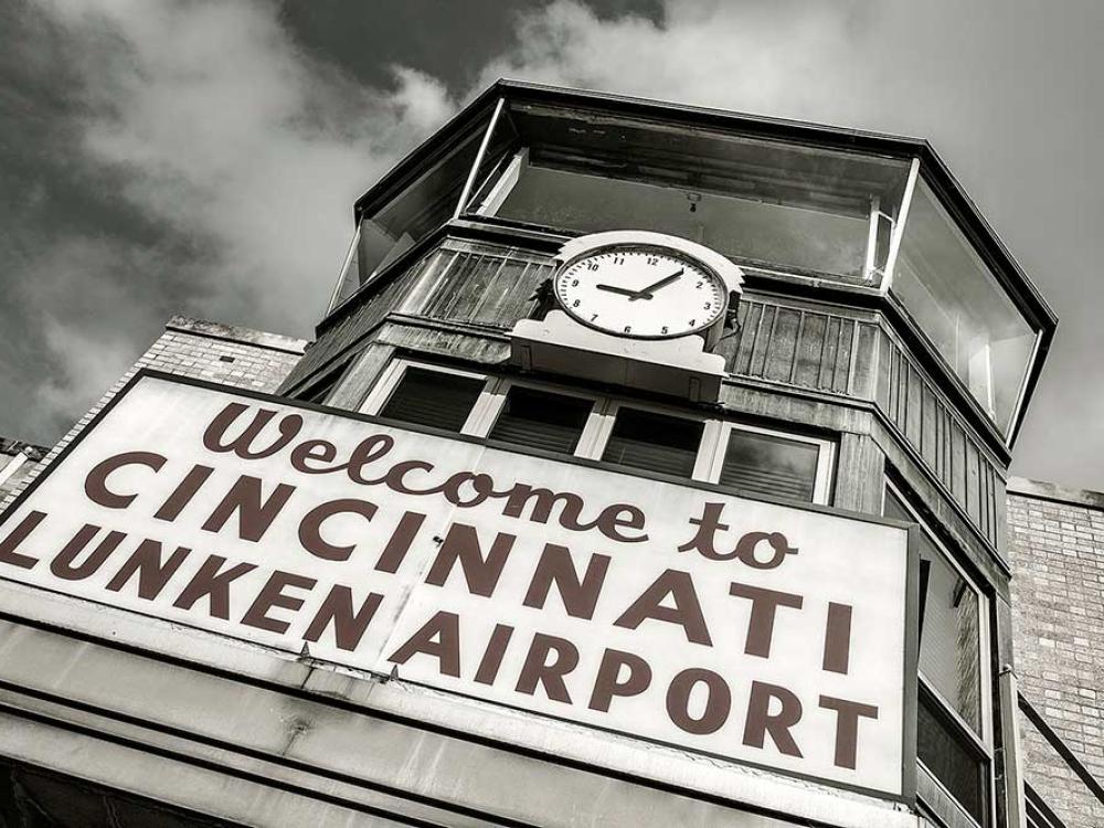 Front view of an air traffic control tower at Cincinnati Municipal Airport. The base is mostly not visible but a sign stating "Welcome to Cincinnati Lunken Airport" is placed under the windows. Above the windows, a clock is visible.