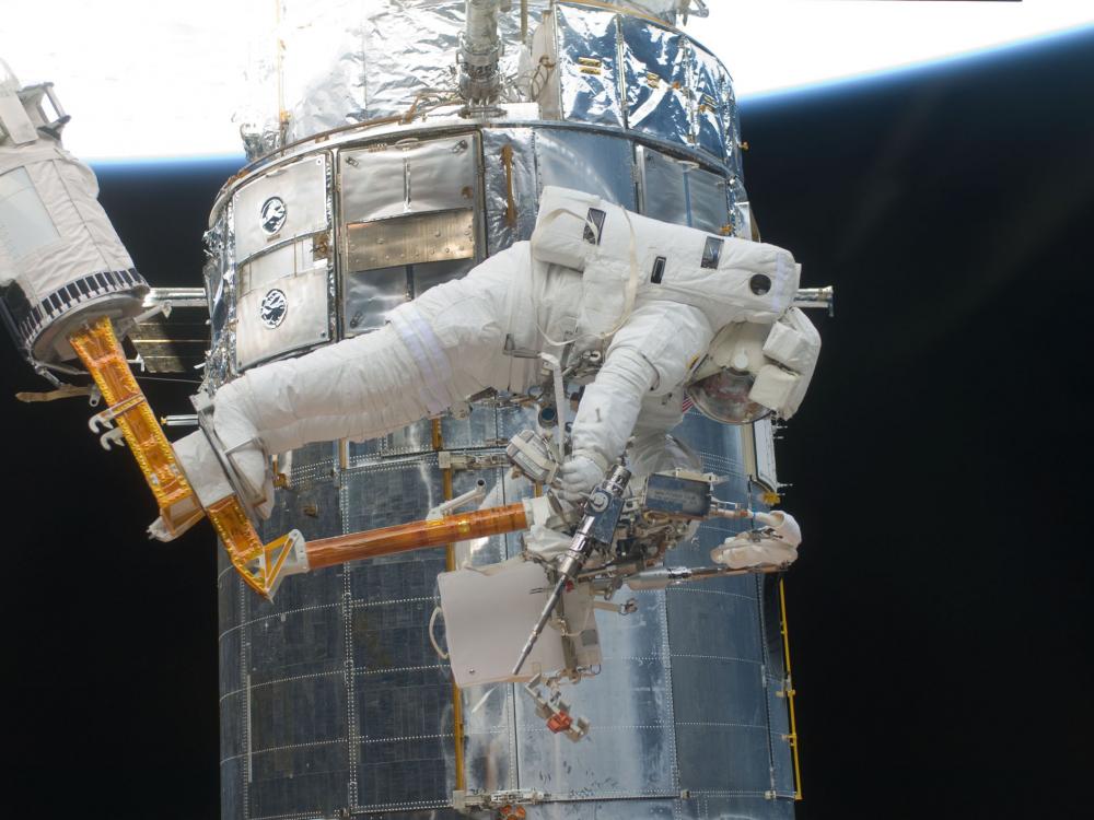 An astronaut during a spacewalk retrieves an object. The astronaut is in a partially prone position.