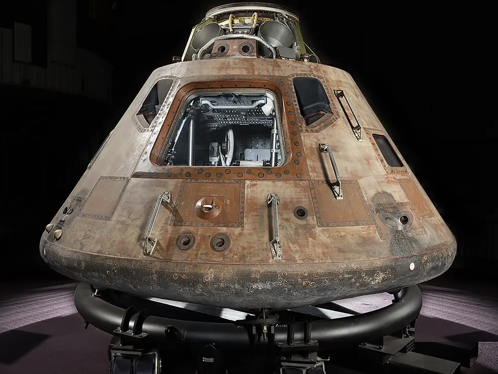 Picture of Apollo 11 Command module Columbia on a transportation rig. Module is lit from above and hatch is facing the camera.