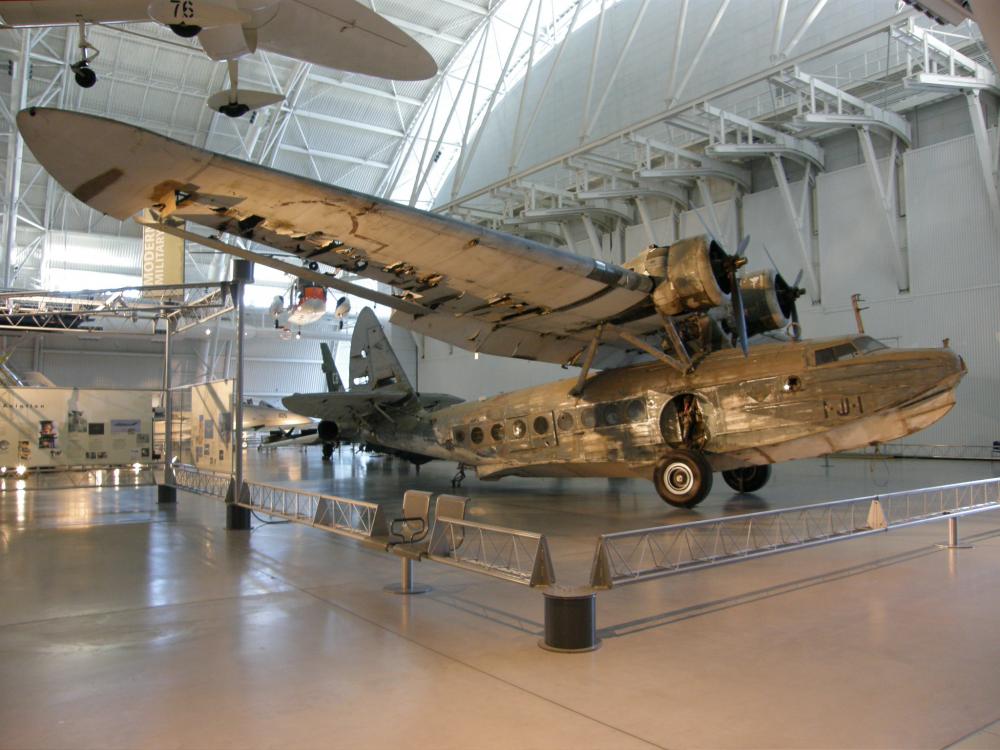 Side view of amphibious seaplane on display at the museum. The aircraft has two engines and its sole pair of wings attached above the plane.