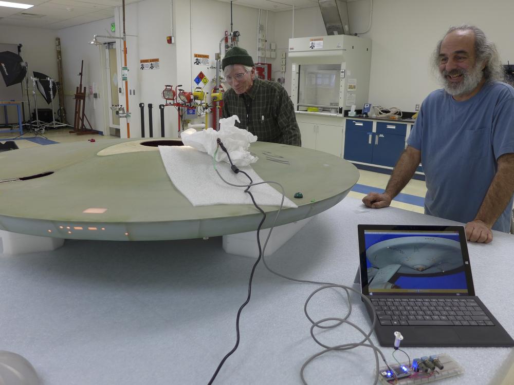 Two Museum specialists test lighting to match the original lighting as part of a gray spaceship studio model used in the Star Trek television series.