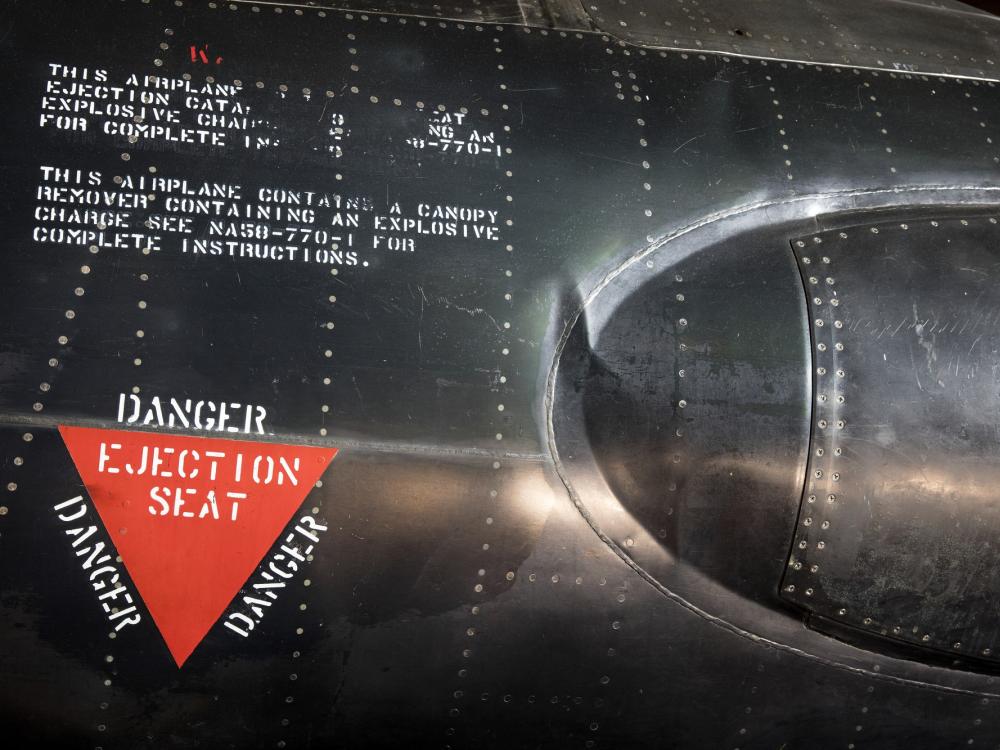 Red triangle "Danger Ejection Seat" label on side of black titanium North American x-15 aircraft