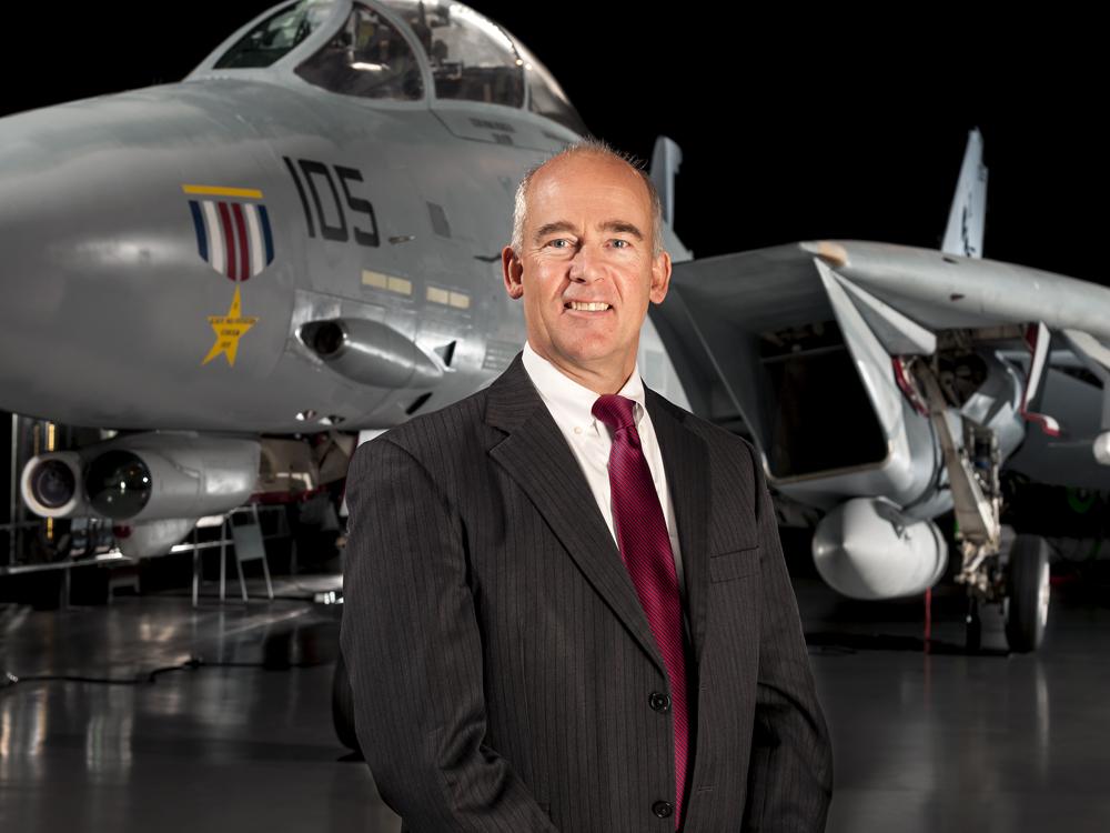 Portrait shot of a man in a suit standing in front of aircraft in a museum setting.