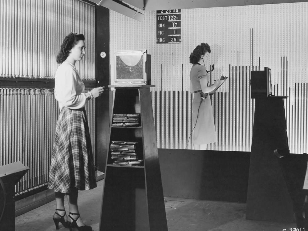 Two women stand at larger boards. 