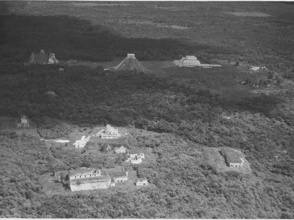 A black and white photograph of tall pyramid like Mayan ruins emerging from a lunch jungle forest.