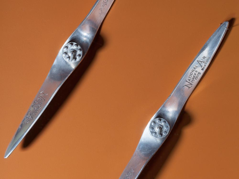 Two metal miniature propellers against an orange-red backdrop. 