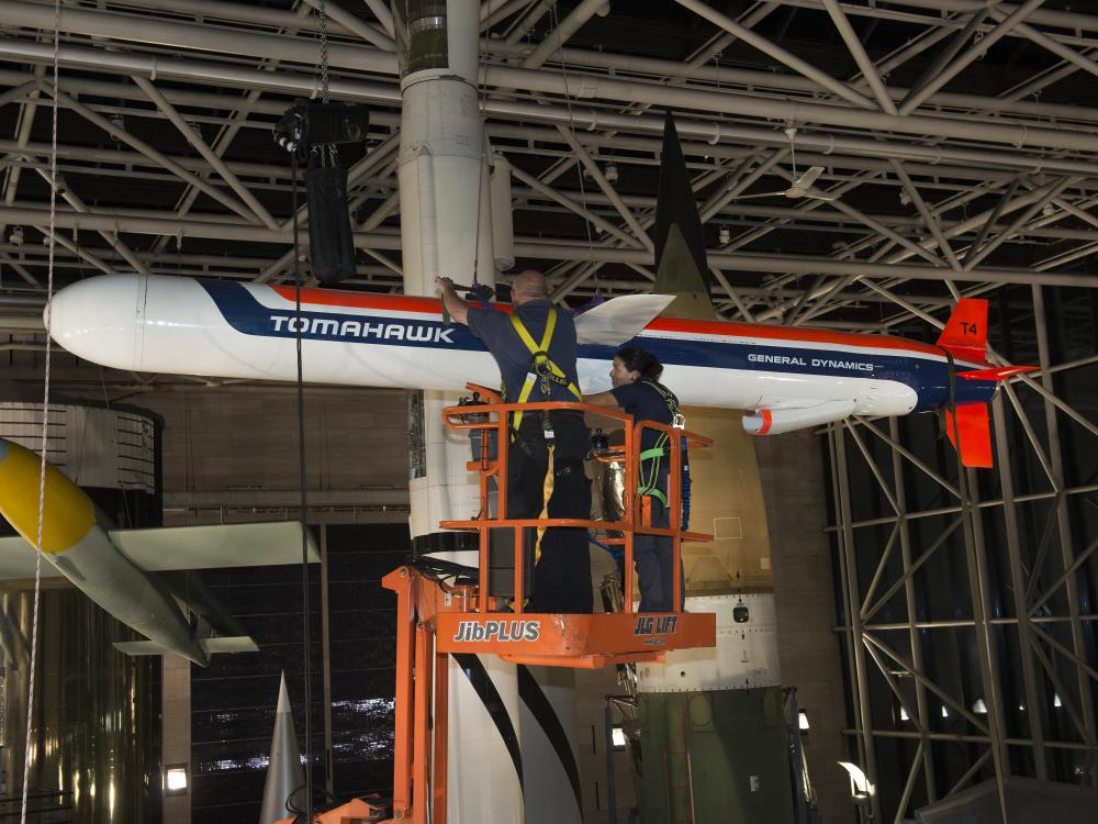 Staff on a lift work to lower a missile attached to the ceiling. 