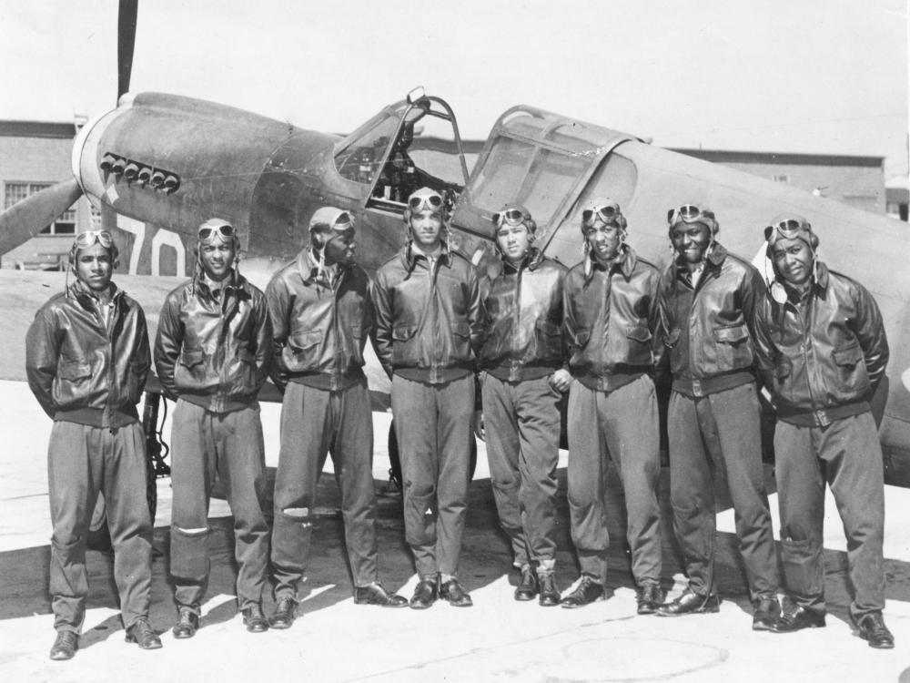 Eight men in jackets and aviation goggles in front of aircraft