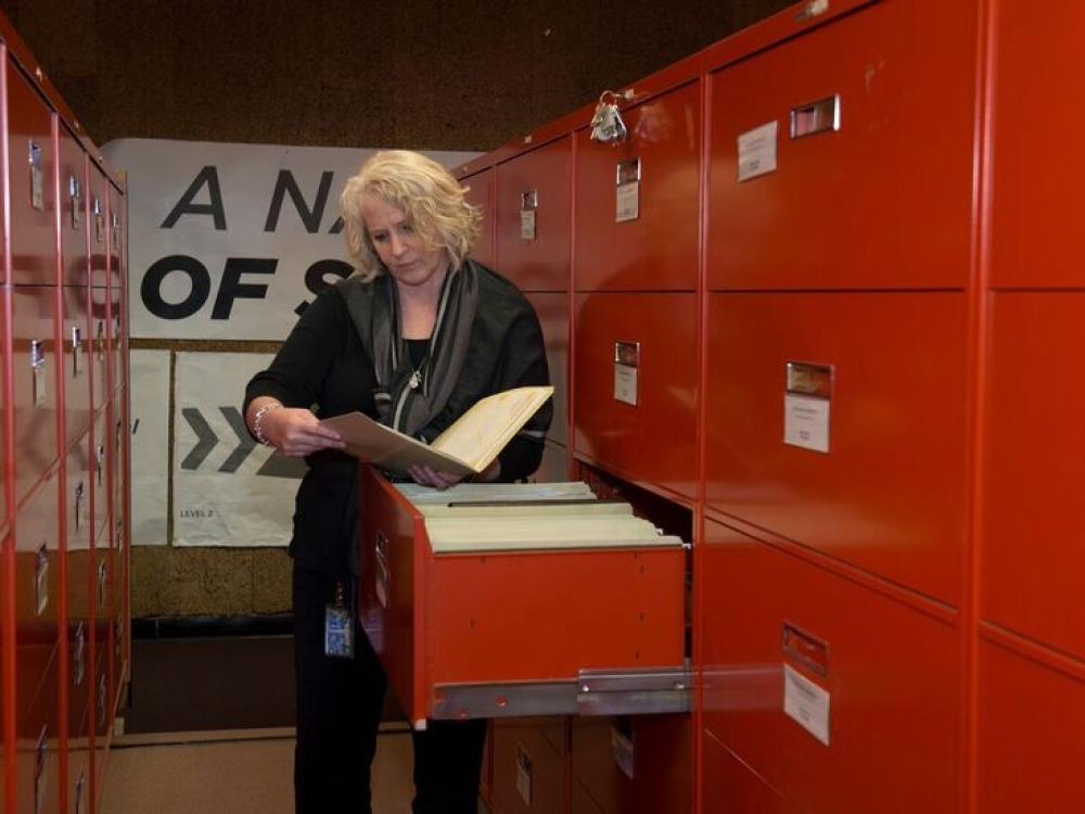 An archivist looks at a file while standing in front of a filing cabinet