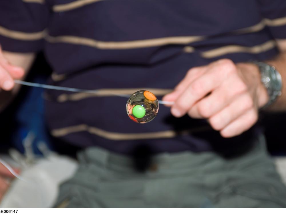 A photo of a water bubble with candy trapped inside floats freely on the middeck of Space Shuttle Endeavour.