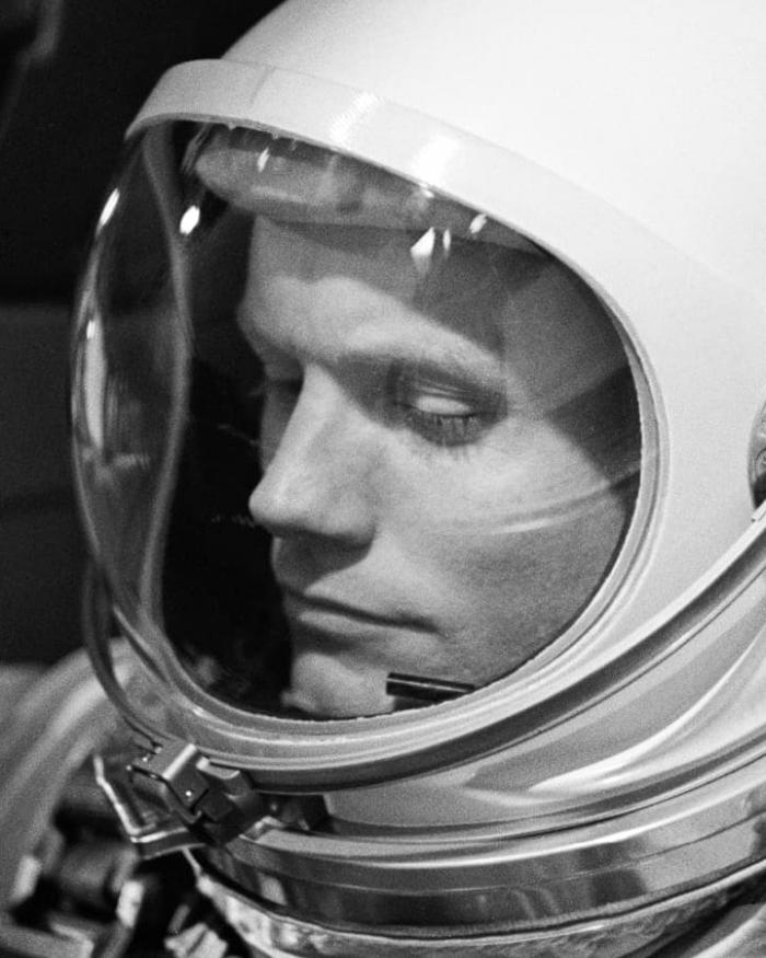 A man in a spacesuit helmet looks down. 