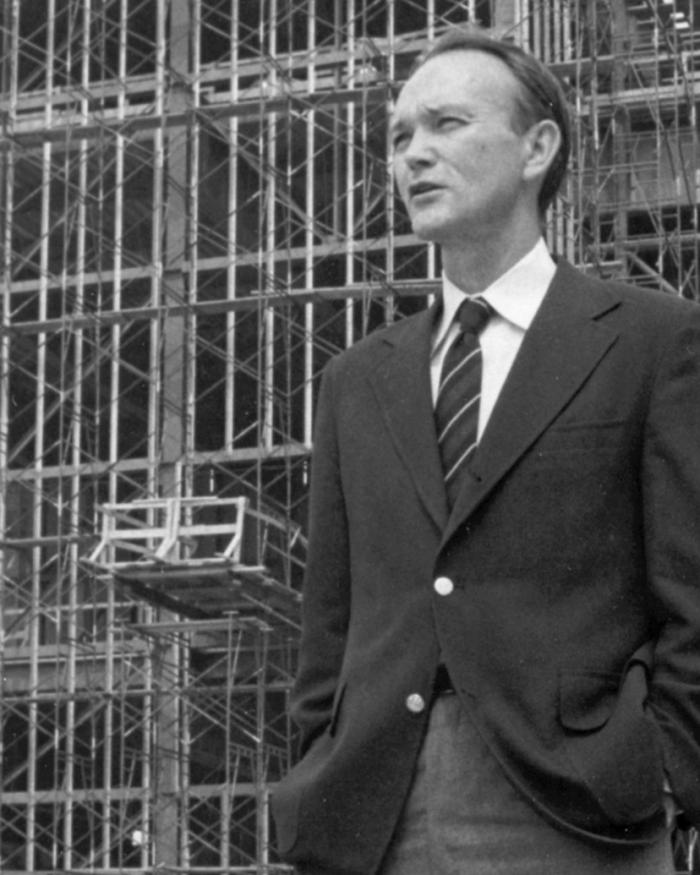A black and white photograph of a man standing in front of construction. 