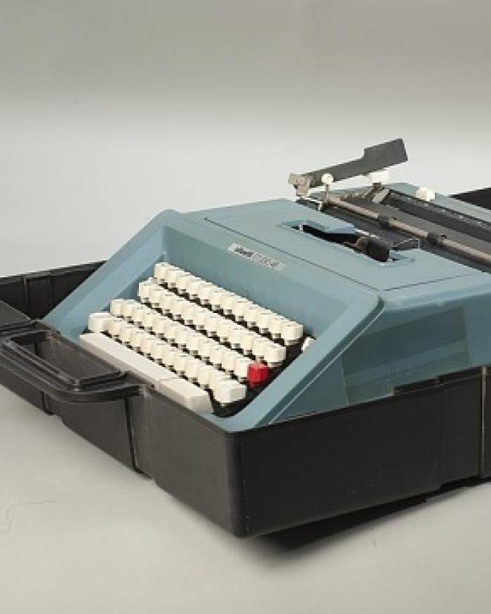 A blue typewriter with white keys and a red tab key, in a box. 