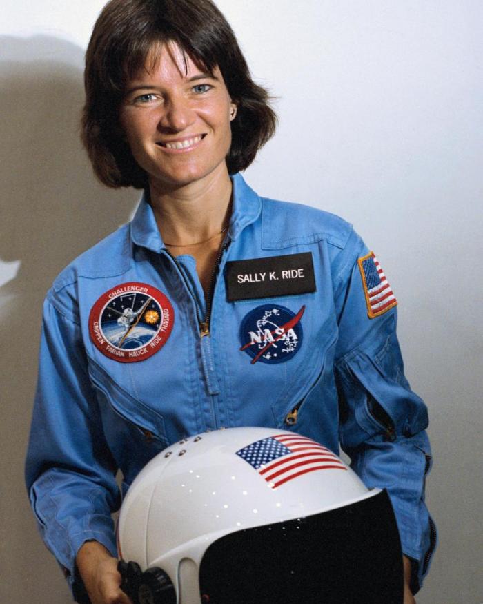 Sally ride in a blue astronaut jumpsuit holding a helmet