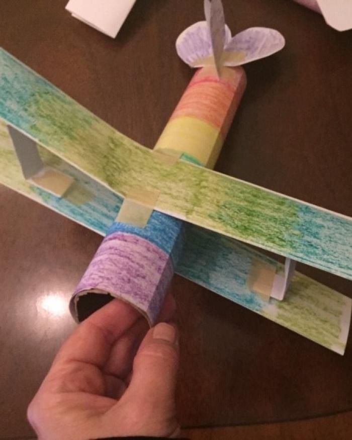 A small plane made from a paper towel roll, colored multiple colors. 