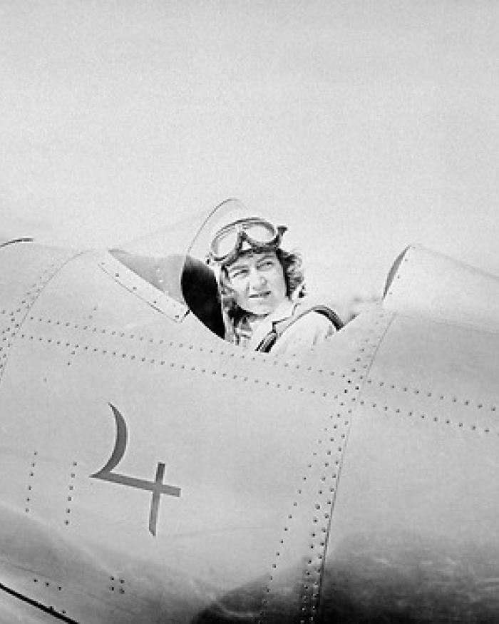 A woman in the cockpit of a plane looks behind her.