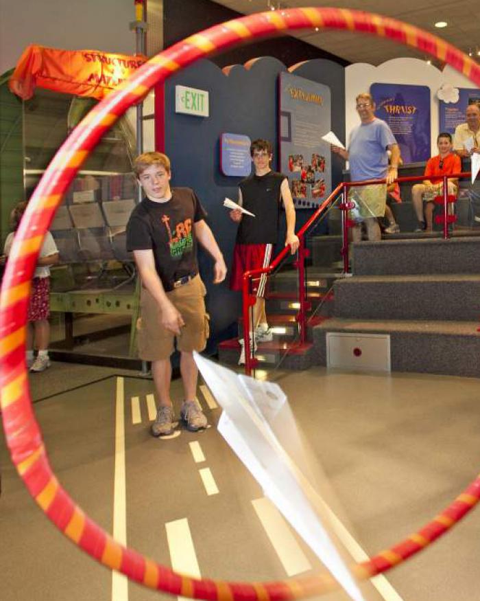 A young man throws a paper plane through a hoop. 