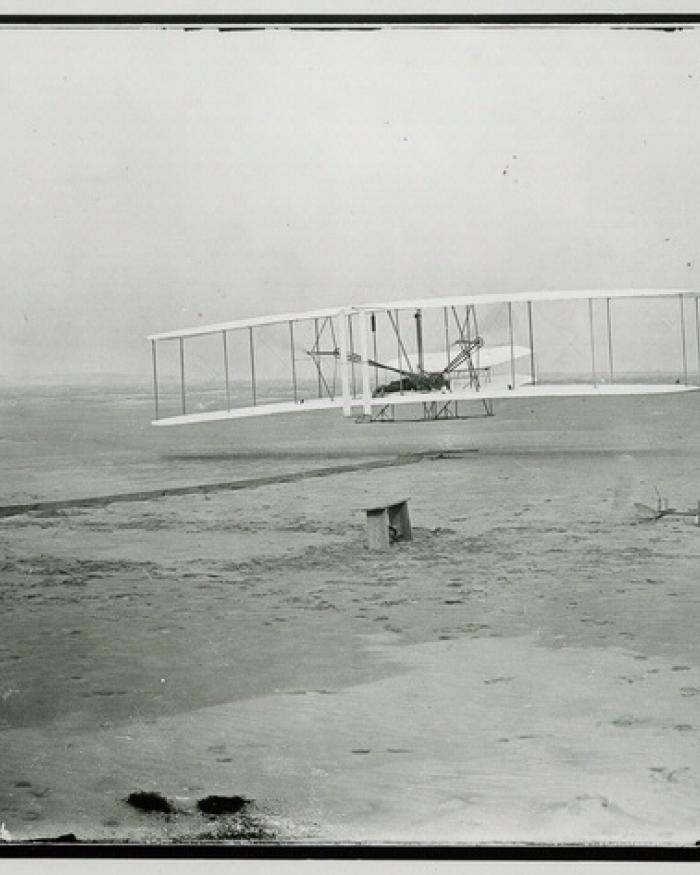 A biplane just barely above the ground with a person standing to the right of it.