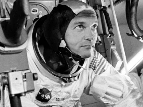 A man, Michael Collins, in a space suit looking out. 