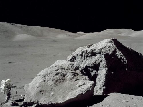 An astronaut by a huge rock on the moon.