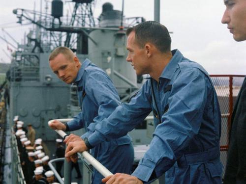 Three white men lean over the railing of a ship.