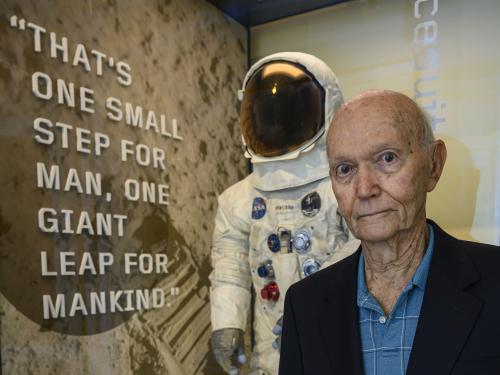 Man in blue shirt stands in front of exhibit case with spacesuit inside.