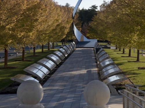 Tree lines path with a vertical swooping metal sculpture at the end