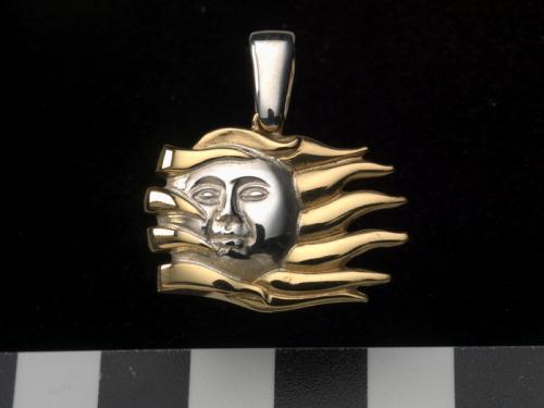 A silver and gold pendant that resembles the rays of the Sun with a face in the center.