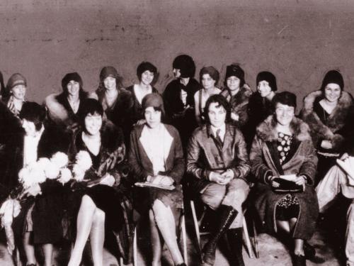 Several women in 1920s fashion smile at the camera in a group portrait. 