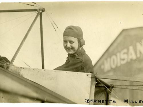 A woman smiles from the cockpit of an airplane.