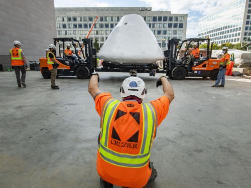 Apollo 11 command module Columbia being lifted by two forklifts and surrounded by workers.