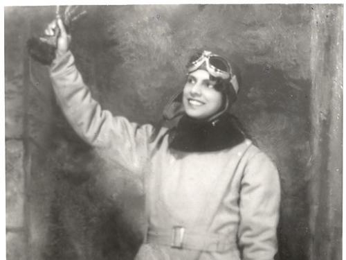 A woman in a flying suit raises her hand in the air.