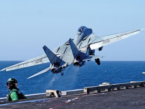 Tomcat aircraft taking off from aircraft carrier. Ocean waves visible below.