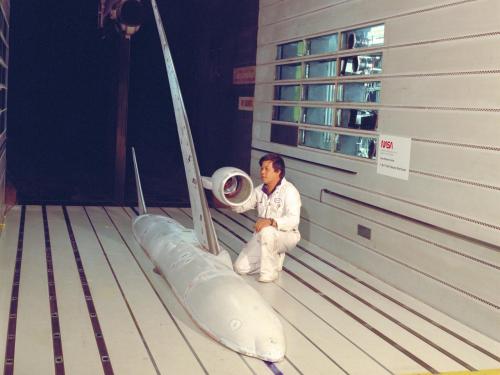 A photo of a man in a wind tunnel with a model of an airplane.