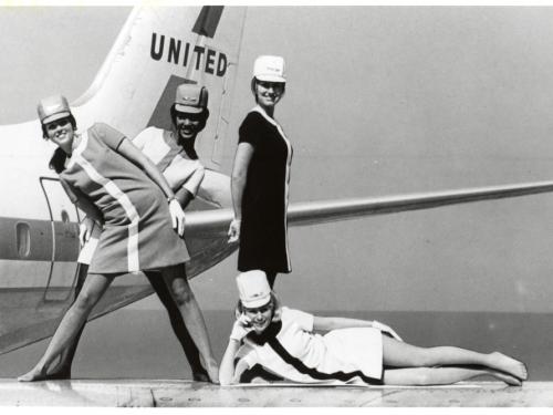 A black and white photograph of four female flight attendants posing in various positions in front of an aircraft.