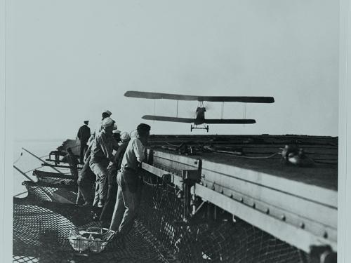 Biplane approaching an aircraft carrier landing deck.