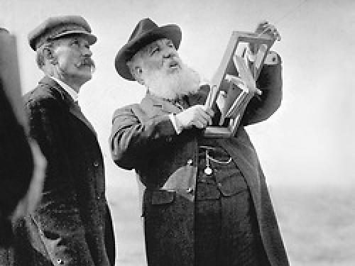 Alexander Graham Bell holding the handle of a kite and looking up into the air.