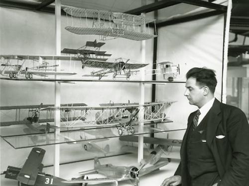 Paul Garber dressed in a suit looking at a cabinet containing airplane models.