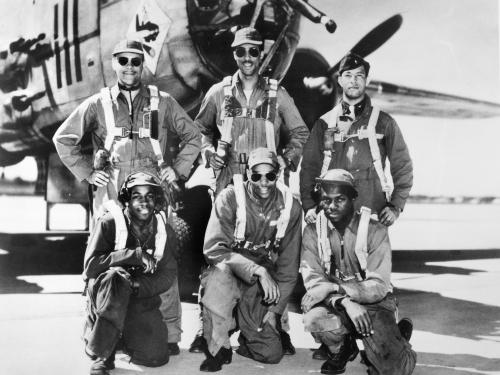 Black and white photograph of six Black men in flight gear (three in front and three in back) posing in front of an aircraft nose.