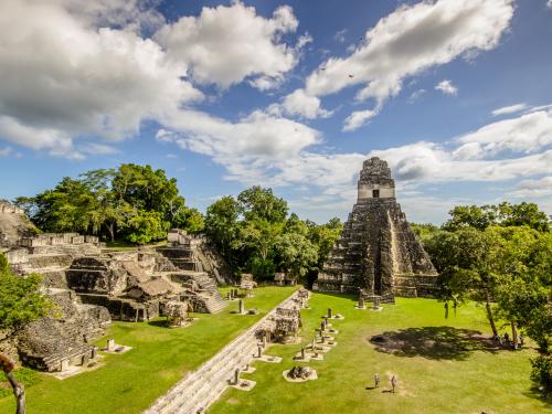 Ruins of ancient city of Tikal, with a large pyramid-shaped temple and several smaller dwellings on the grounds around it.