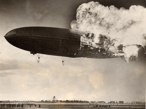 An airship is seen with the back half of its body on fire as it is still in the air.