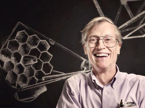 Man wearing glasses and purple shirt in front of a chalk sketch of the James Webb Space Telescope