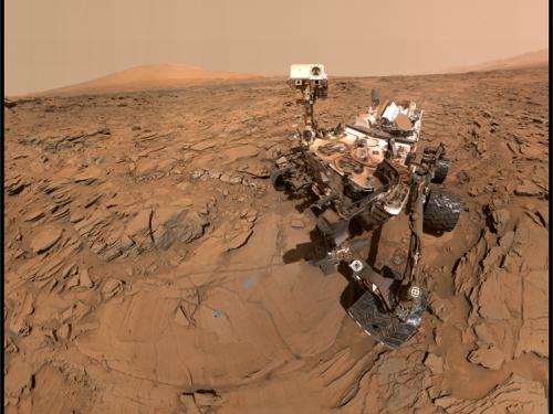 A rover takes a photograph on the orange, dusty martian surface. 