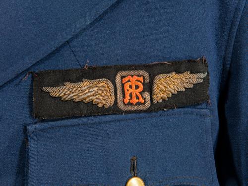 A black patch embroidered with gold wings which have the letter R and T on top of each other at the center.