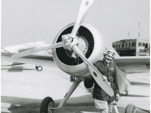 View of the Turner-Laird LTR-14 "Pesco Special" on the ground; pilot Roscoe Turner, in uniform, poses standing behind one blade of propeller at left side of nose of the aircraft.